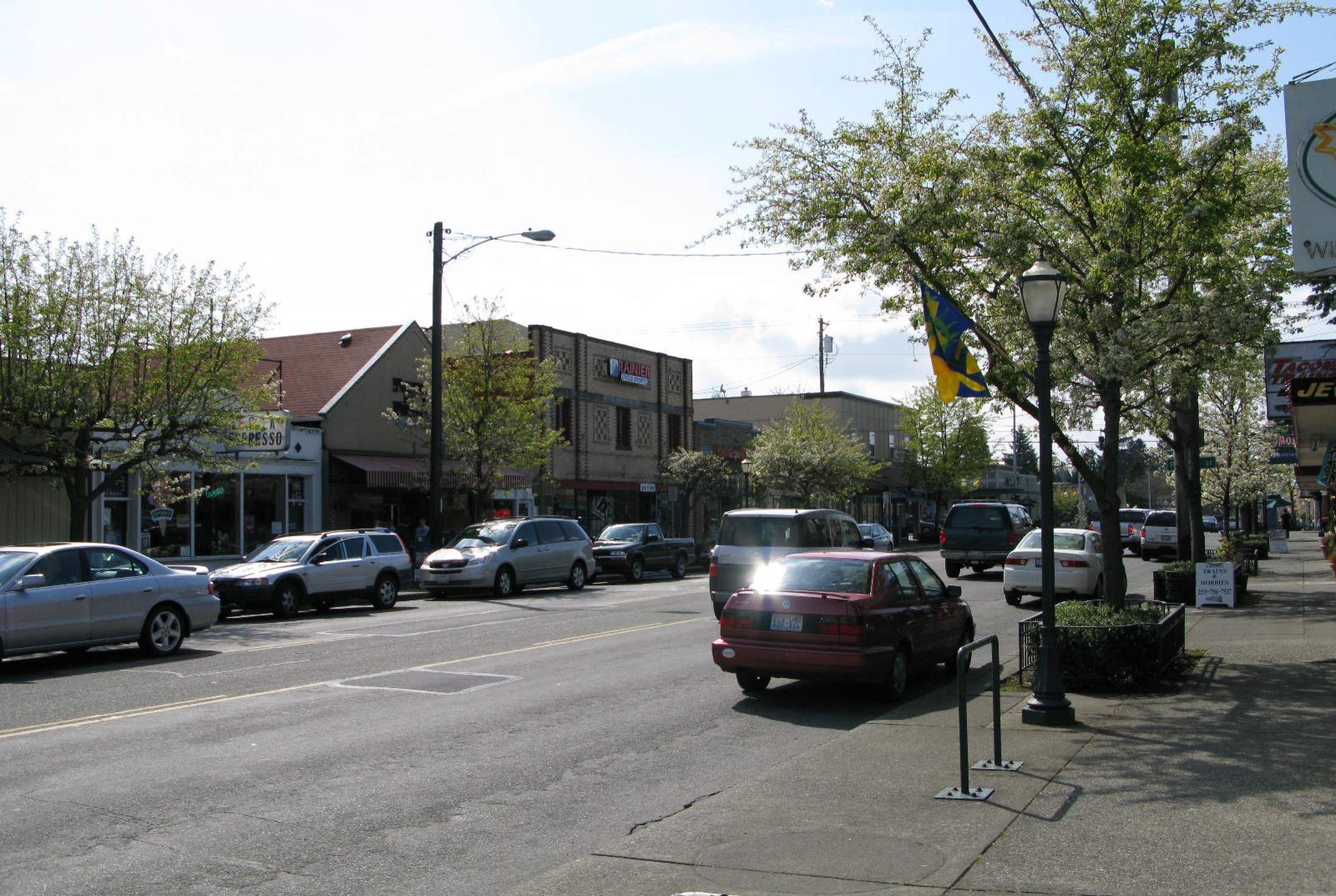 North 26th Street in Tacoma's Proctor District, with storefronts, street trees, and parked cars on a spring afternoon